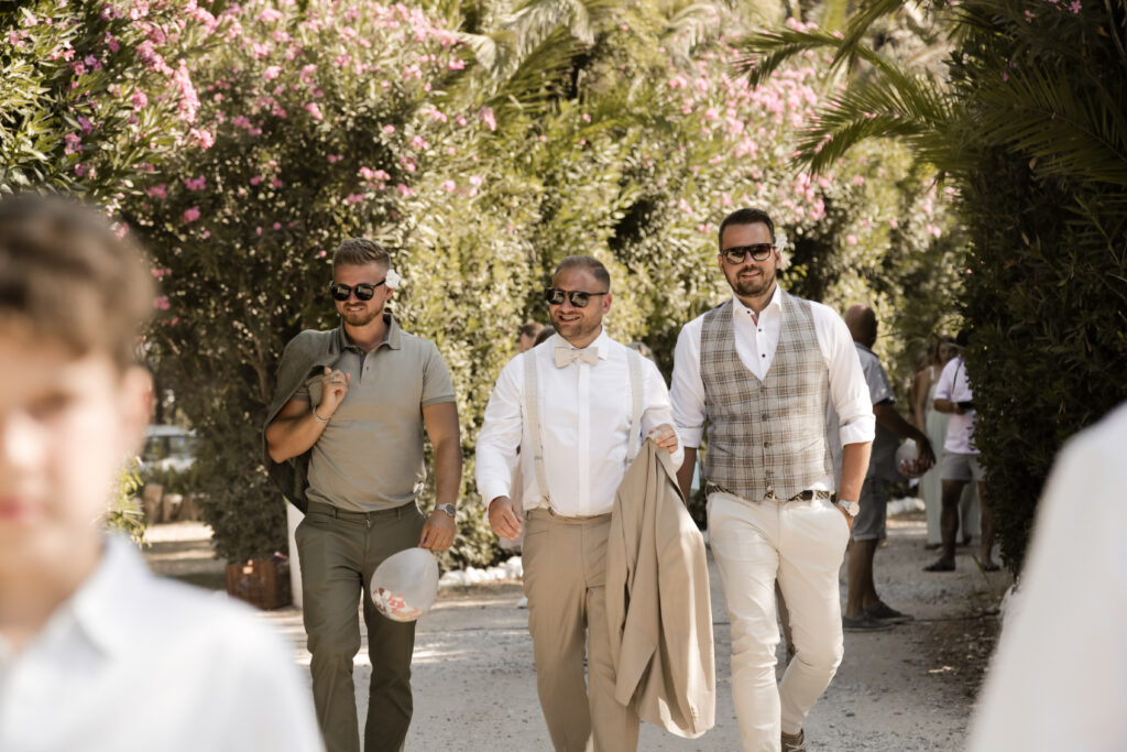 Brüutigam und Trauzeugen spazieren zur Hochzeit am Strand auf Kreta in Griechenland.