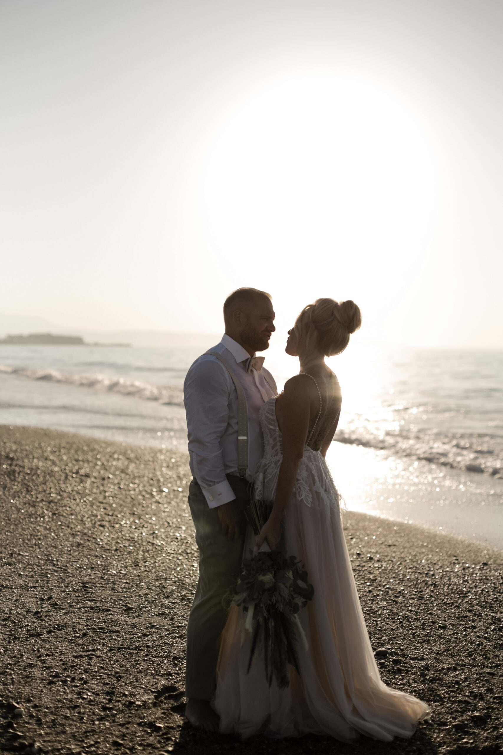 Brautpaar steht im Sonnenuntergang Licht der goldenen Stunde am Meer nach Trauung Hochzeit zum Fotoshooting auf Kreta bei Rethymno